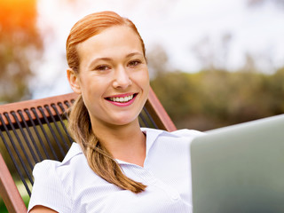 Young business woman sitting in park and working with laptop