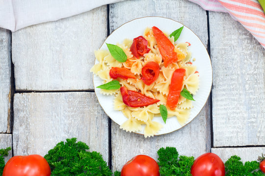 Vegetarian Vegetable pasta farfalle with tomto, peppers and basil in white plate on wooden table. Top view