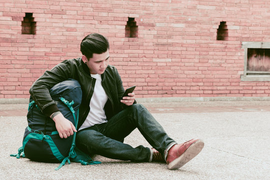 Asian Traveler Man Sitting On The Street And Using Smartphone.