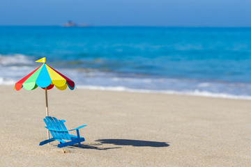 beach umbrella and chair made from paper standing on sand on background of blue ocean. The hot climate. Handmade.