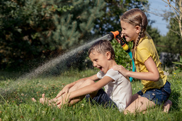 Happy kids sitting on the grass and pouring water from a hose.