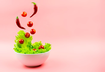 Salad, cherry tomatoes and chili peppers flying out of the white bowl on a pink background. Concept of a healthy diet. Selective focus, copyspace.