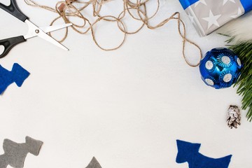 Festive background of Christmas present decoration. Felt fir tree, ornament ball, gift box and scissors with string, top view and copy space. Holiday preparation, home and restaurant decor concept