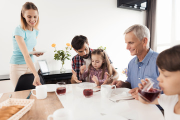 The woman arranges the plates before her family, who is waiting for dinner and is already sitting at the table
