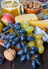 Autumn set of products: grapes, walnuts, hazelnuts, plums, honey, cheese, raisins, pears, dried cranberries on a wooden background