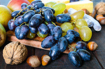 Autumn set of products: grapes, walnuts, hazelnuts, plums, honey, cheese, raisins, pears, dried cranberries on a wooden background