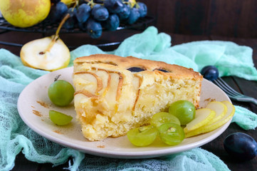 A large piece of a pie with pears and grapes on a plate on a dark wooden background.
