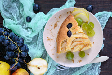 A large piece of a pie with pears and grapes on a plate on a dark wooden background.