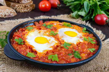 Shakshuka - a dish of eggs fried in a sauce of tomatoes, hot pepper, onions and seasonings. Israeli cuisine. Served for breakfast with rye bread.