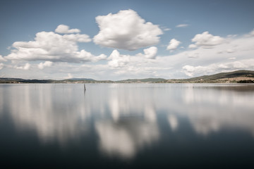 Long exposure view of a lake with moving white clouds perfectly reflecting on water