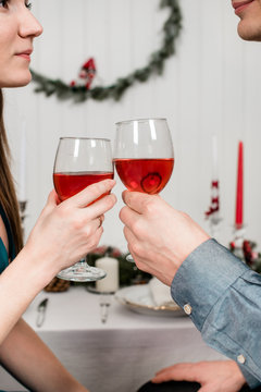 A close picture of young spouses clinking glasses and looking at each other. Beautiful couple sitting at the laid table for thanksgiving day, holding glass of wine in the hands.
