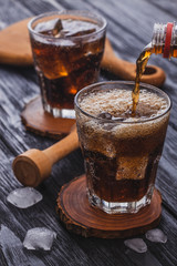 cola with ice in a glass on a black wooden table.