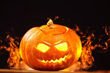 Closeup jack-o-lantern Halloween pumpkin with fire burning around at dark background.