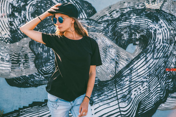 Model wearing plain tshirt and sunglasses posing over street wall