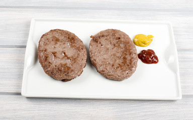 Burgers on white plate with ketchup and mustard on wooden table. Food.