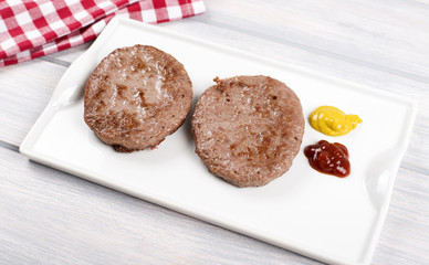 Burgers on white plate next to napkin with ketchup and mustard on wooden table. Food.