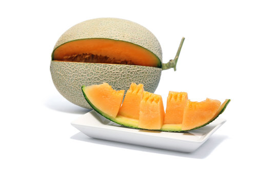 Sliced melon in pieces arranged on white dish and melon fruit on white background.