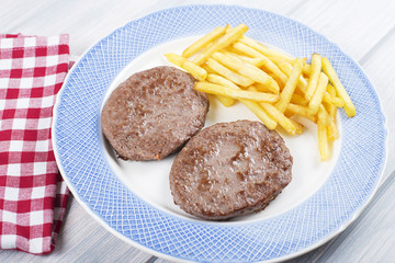 Burgers with french fries on blue plate next to napkin on wooden table. Food.