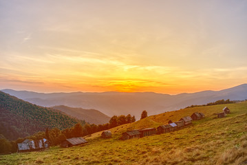Fototapeta premium Beautiful sunset on a blue sky background. On the slope of the mountain there are small wooden houses.