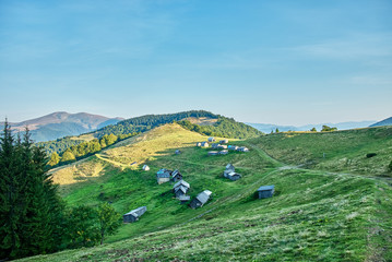 Beautiful sunset on a blue sky background. On the slope of the mountain there are small wooden houses.