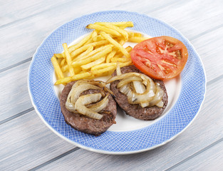 Hamburger with fries, onion and tomato on blue plate next to napkin on wooden table. Food.