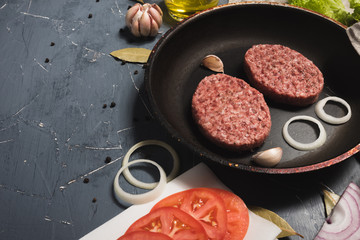 Organic fresh minced meat cutlets. Raw Ground beef meat Burger steak with ingredients in a frying pan on grey background