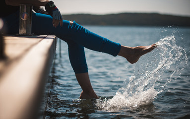 A happy young girl is kicking feet on a sea pier and splashing water