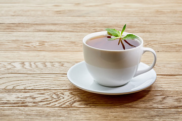 Cup of mint tea and green leaves on light table