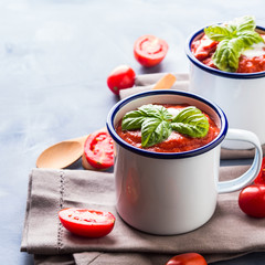 Creamy Tomato soup in enamel mugs on blue background
