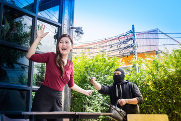 The thief under black mask is intimidating for extortion a beautiful woman's handbag.