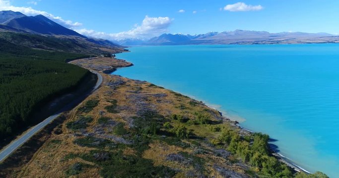 New Zealand aerial drone video of lake Pukaki and southern alps on South Island. Road and clear blue lake and sky with Aoraki / Mount Cook National Park in background. New Zealand Tourist destination