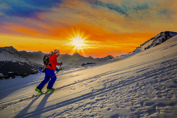 Mountaineer backcountry ski sunrise walking up along a snowy ridge with skis. In background cloudy...