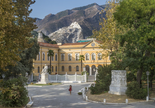 A lonely woman walks in the park of the library Biblioteca Civica Cesare Vico Lodovici, Carrara, Italy, with the mountains and the famous marble quarries in the background