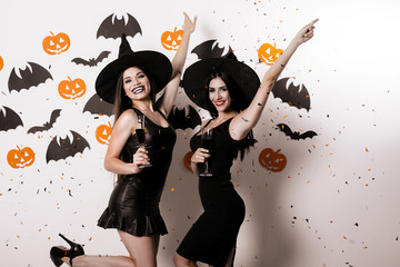 Two women in suits witches posing against a background of paper bats. Confetti is on them and they smile