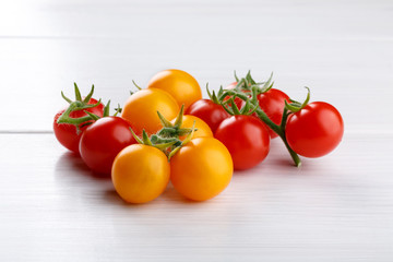 Heap of red and yellow small cherry tomatoes on white table.