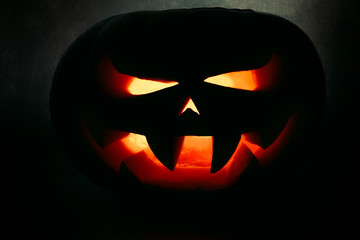 A very terrible Halloween pumpkin, with a terrible look and a smirk of a villain, in the dark
