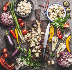 Kitchen table with chopped eggplant on wooden cutting board with knife and various vegetarian...
