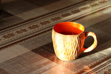 Orange ceramic handmade cup with tea on the table in the rays of the setting sun