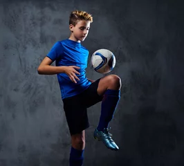 Tuinposter Teenager soccer player dressed in a blue uniform plays with a ball. © Fxquadro