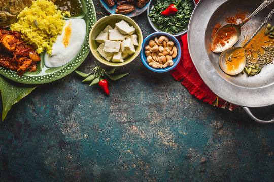 Various indian food bowls with curry, yogurt ,rice,bread , chicken,chutney, paneer cheese and spices on dark rustic background, top view, border