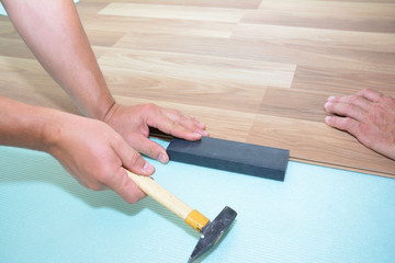 Contractors installing wooden laminate flooring with insulation and soundproofing sheets. Man laying laminate flooring. Man laying laminate flooring.