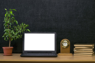 Teacher or student desk table. Education background. Education mockup concept. Laptop with blank screen, plant in the pot, stacked books and clock watch on blackboard (chalkboard) background.
