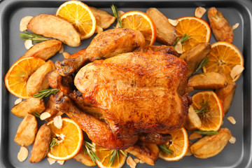 Roasted turkey with slices of orange and potatoes on baking sheet