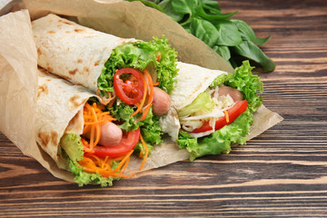 Tasty lavash rolls with sausages and vegetables on wooden table