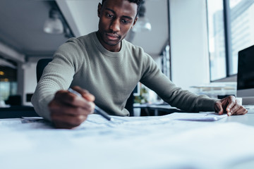 Young man working on blueprint at desk in office