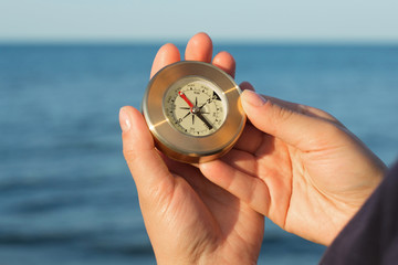 Hands holds a little compass indicating the direction on the background of the sea