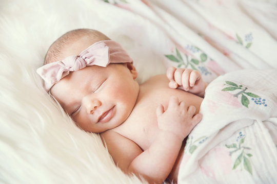 Sleeping smiling newborn baby in a wrap on white blanket.