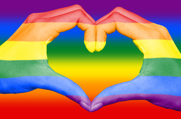 Gay rainbow flag painted on hands forming a heart on rainbow background, LGBT love and pride month...