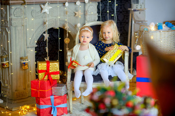 two happy girls are sitting on a chair and holding boxes with gifts
