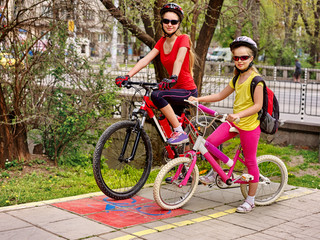 Obraz premium Family bike ride in autumn. Mother and daughter wearing bicycle helmet with rucksack. Children biking on yellow bike lane. Child in foreground teenager on background. Children travel unaccompanied.